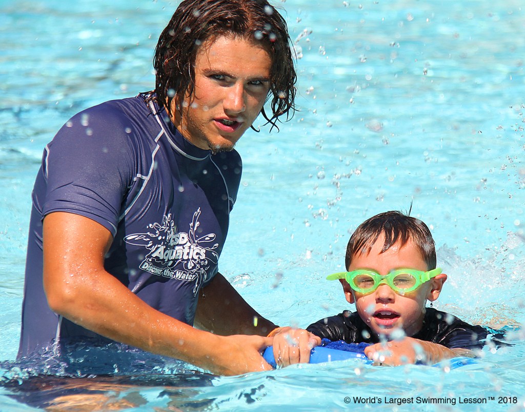 Each year, WLSL events provide more than 20,000 man hours of water safety training in a single day. Here, a lifeguard at the Jerry Fox Swim Center teaches a young child how to swim using a kick board.