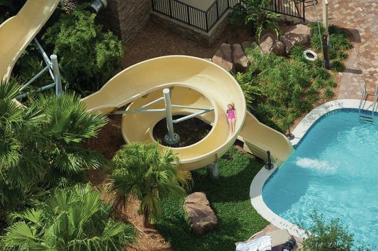 The facility includes a pool with multiple zero entries, a grotto pool with large rock waterfall, a pool with single-rider slide tower, interactive wet deck with LED lighting, and a children’s play pool. An aquatic wellness area accompanies the spa, and multiple waterfeatures punctuate the property.