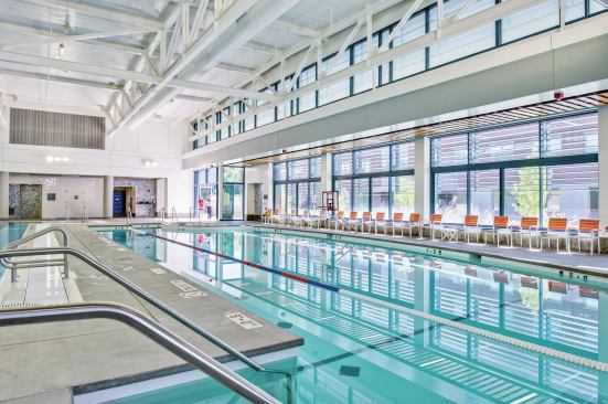 Keeping in mind that Boise enjoys sun more than 200 days per year, the design team created the nearly 18,000-square-foot facility to take advantage of as much natural light as possible and connect with the environs. Large, operable windows on three sides provide a direct visual connection to the outdoors. A continuous skylight creates shadow patterns, and clerestory windows bring in reflected daylight, which balances the space. In warm weather, a large sliding door can open and create a connection to the outdoor terraces. The windows and skylight also provide ventilation when weather allows, thereby adding to energy efficiency. To that end, the team also had solar panels installed on the roof to aid with the pool heating and HVAC system. Blue mosaic tiles on the vertical surfaces echo waterfeatures, while the white of the ceilings, structure and high walls put the focus where it belongs — on the blue water.